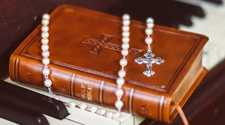 White Rosary and a brown leather Bible on a piano