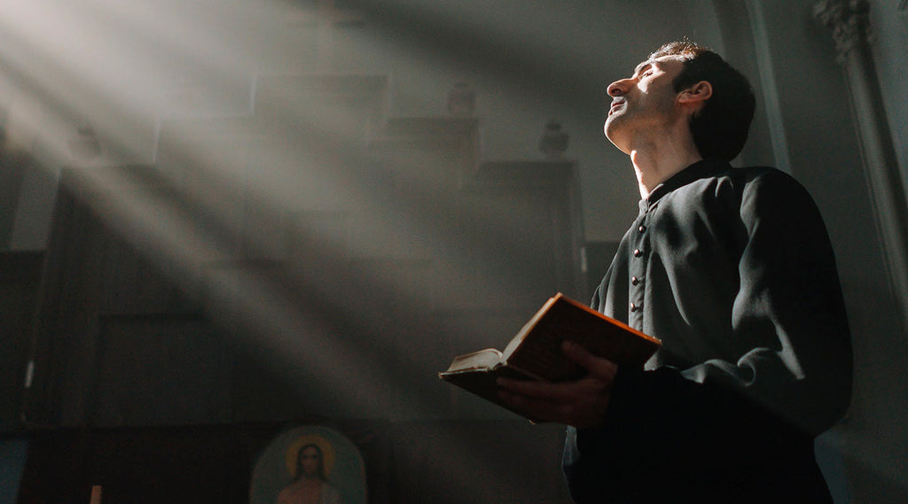 Priest wearing black robe and holding The Bible praying in church