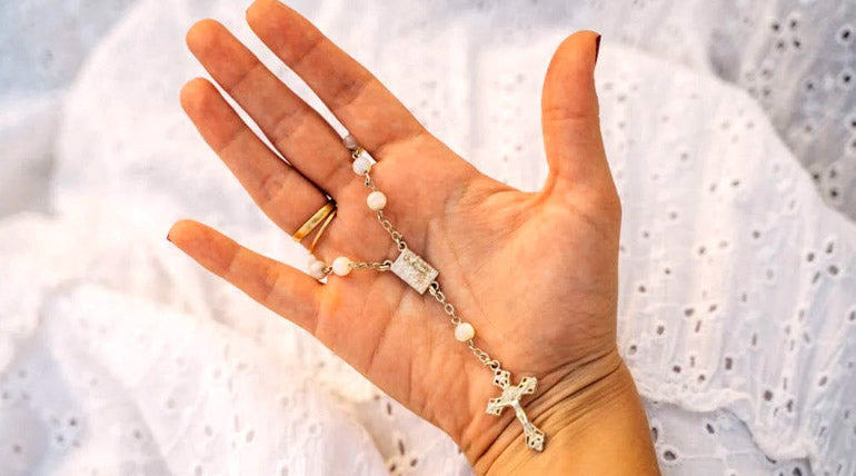 Woman´s hand holding a golden rosary on a white background