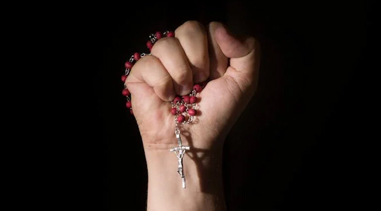 Red rosary made of rose petels held in a hand on a black background